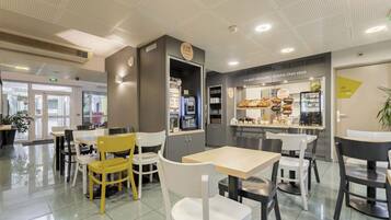 A café with tables and chairs, a refrigerator, and a display of baked goods.