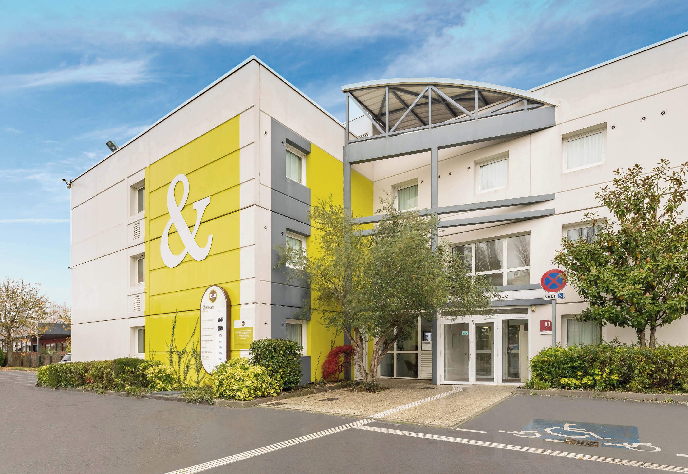 A modern building with a prominent "&" sign on the facade, a covered entrance, and a parking area with a handicapped parking space.