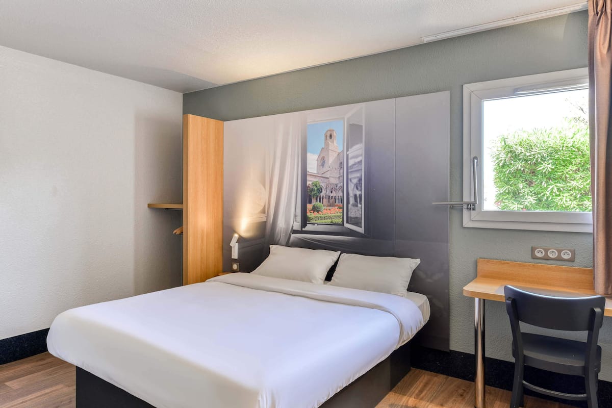 Une chambre d’hôtel avec un lit, un bureau et une fenêtre donnant sur un paysage verdoyant.