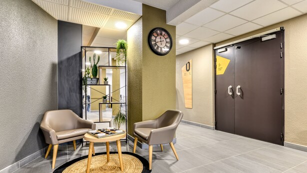 Un vestíbulo con dos sillones de cuero, una mesa redonda, un reloj y una puerta con un letrero.
