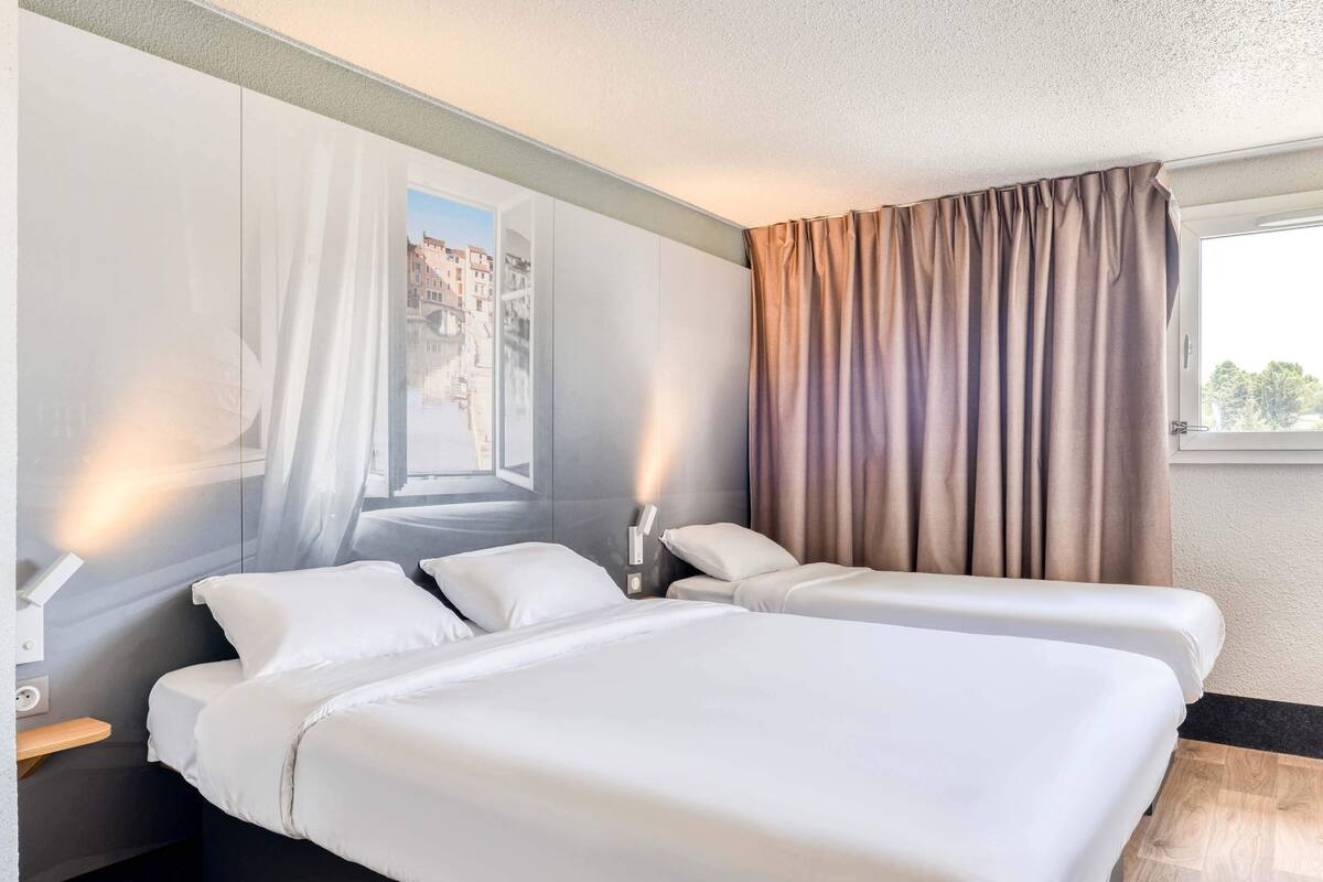 Une chambre d’hôtel avec deux lits, une fenêtre avec des rideaux et un luminaire fixé au mur.