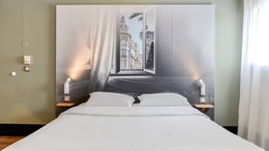 Una habitación de hotel con una cama grande, dos mesitas de noche y una lámpara fijada a la pared.