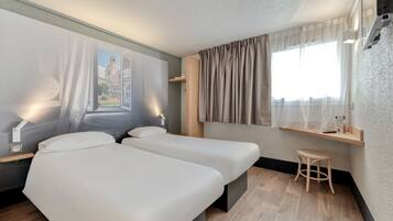 Une chambre d’hôtel avec deux lits, un petit tabouret, une fenêtre avec des rideaux, une étagère fixée au mur et un tableau représentant un bâtiment.
