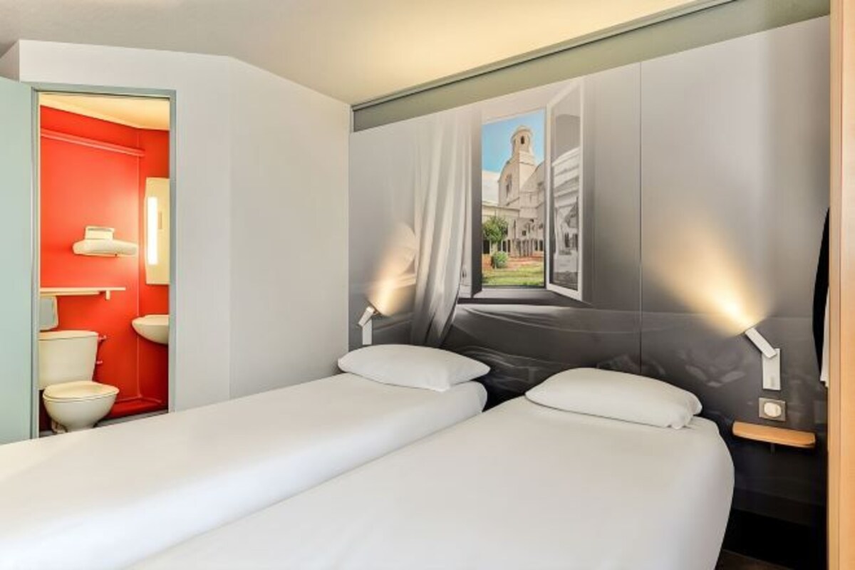 Habitación de hotel con dos camas, un baño rojo y un mural de un edificio.