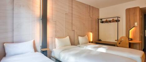 A hotel room with two beds, a wooden headboard, a mirror, and a small table with a chair.