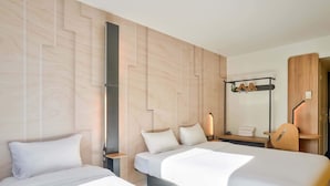 A hotel room with two beds, a wooden headboard, a nightstand with a lamp, and a mirror. - B&B HOTEL Paris Malakoff Parc des Expositions (Malakoff)