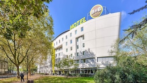 A modern hotel building with a prominent "HOTEL" sign, surrounded by trees and a well-maintained lawn. - B&B HOTEL Paris Malakoff Parc des Expositions (Malakoff)