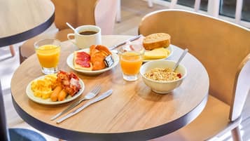 A breakfast table with plates of eggs, toast, and fruit, along with a bowl of cereal and a glass of orange juice.