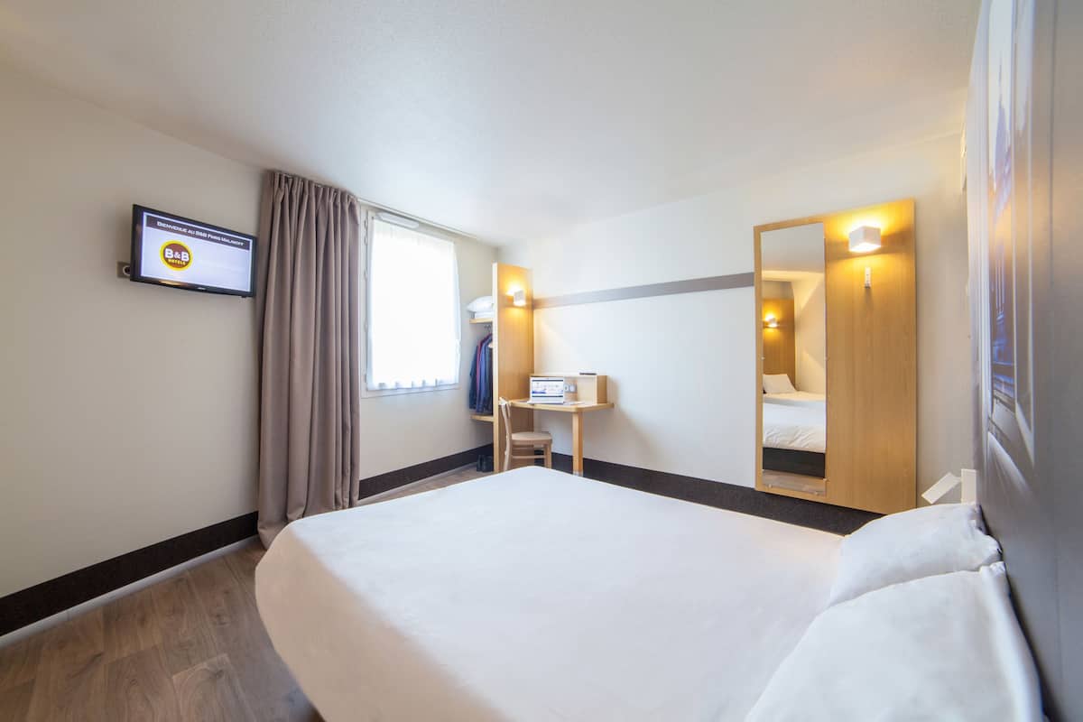 A hotel room with a large bed, a desk with a computer, a TV mounted on the wall, and a mirror.