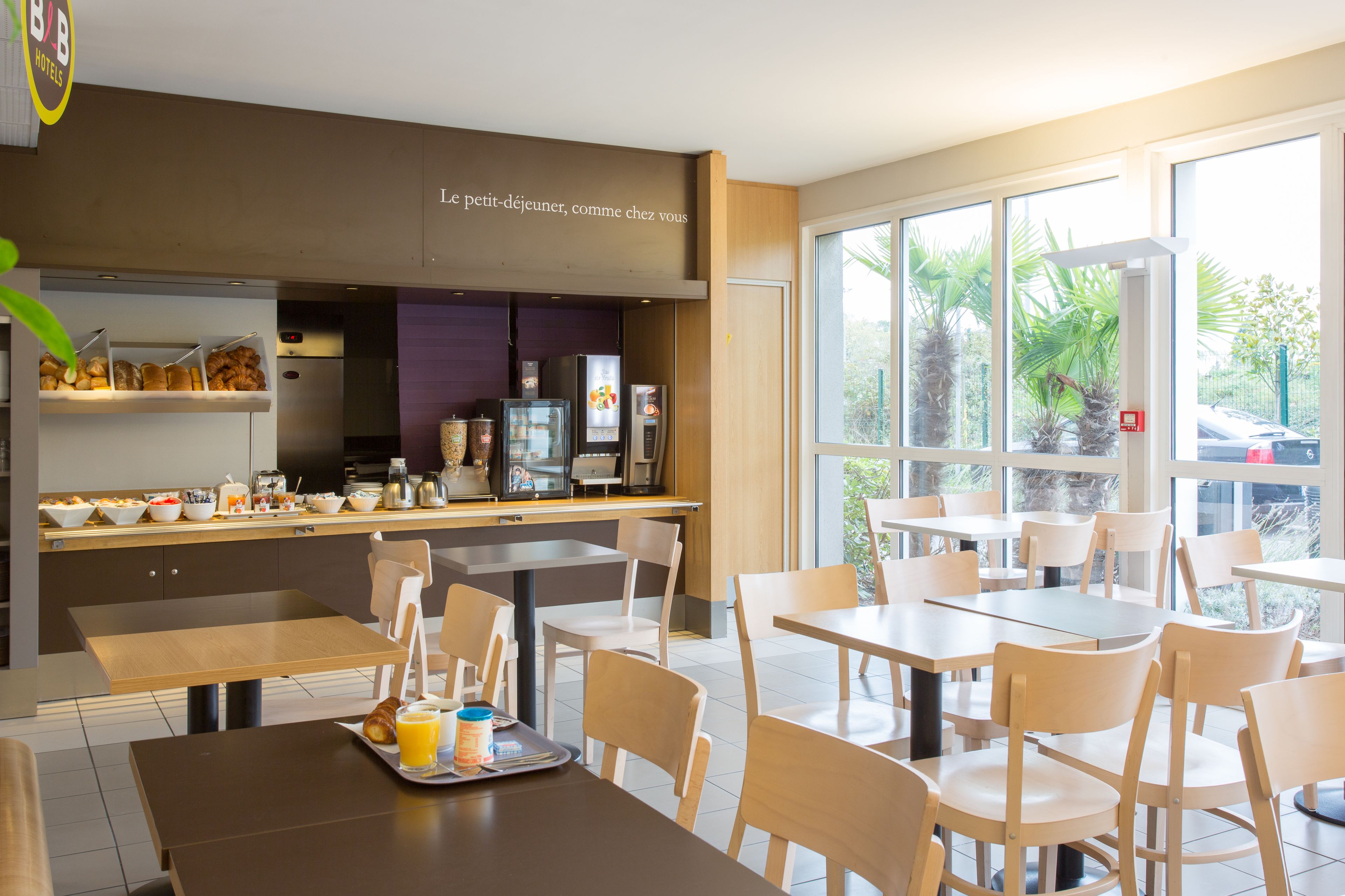 A modern breakfast area with a counter displaying various food items, seating arrangements, and a view of the outdoors.