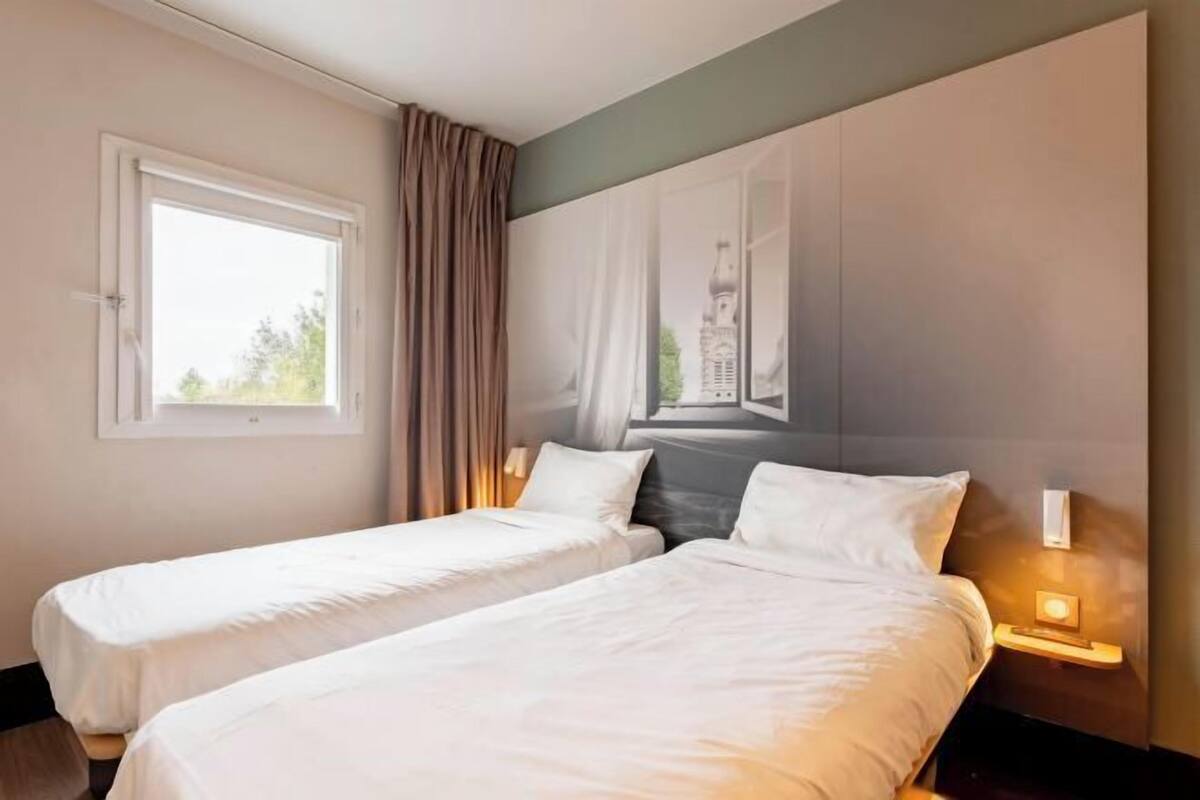 Habitación de hotel con dos camas individuales, un ventanal grande y un mural en la pared.