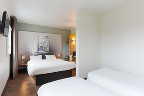 Een hotelkamer met twee bedden, een flatscreen televisie aan de muur, een nachtkastje met lamp en een groot raam met gordijnen.