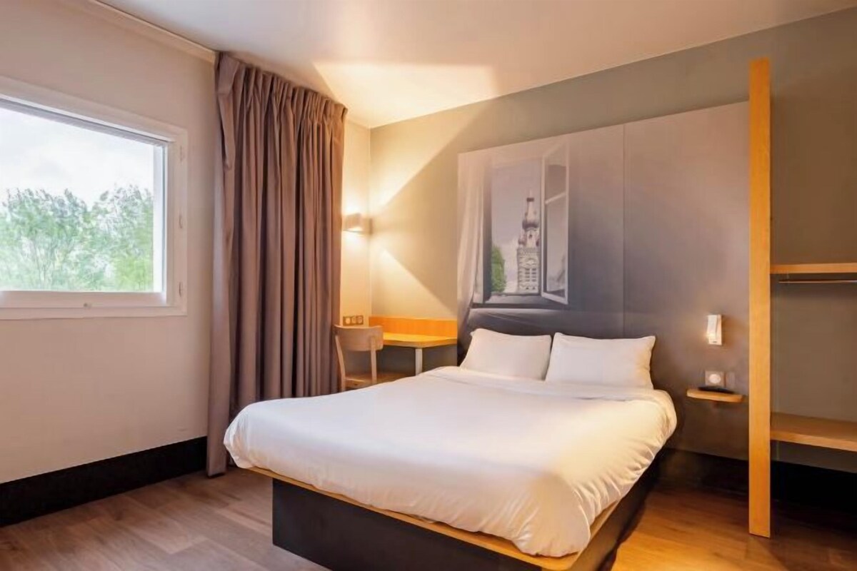 Une chambre d’hôtel moderne avec un grand lit, un bureau et une fenêtre avec des rideaux.