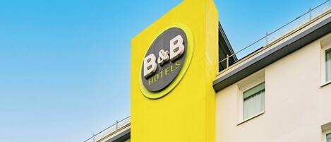 Señal de un hotel B&B en un edificio amarillo, con un cielo azul despejado al fondo.