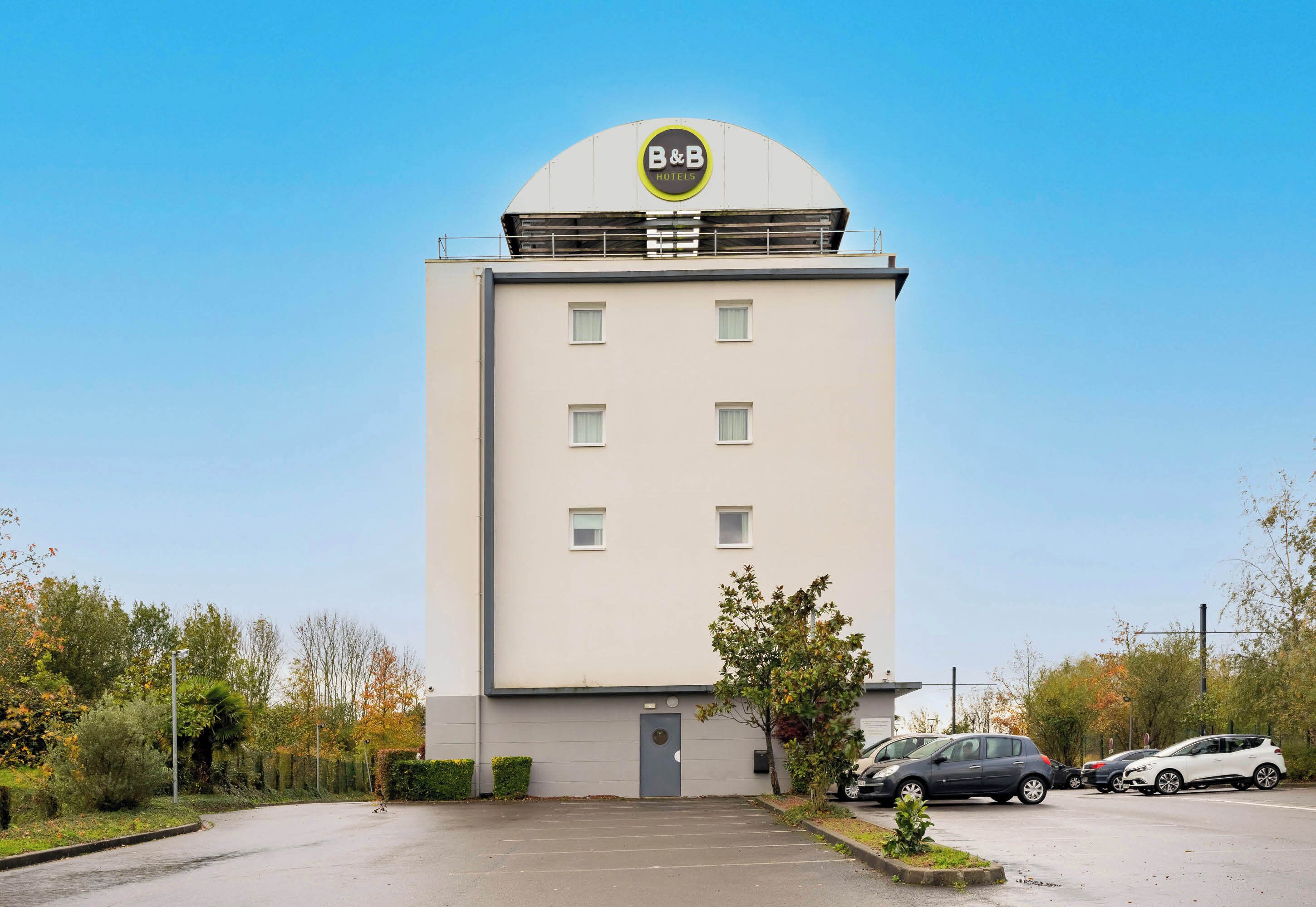 Un hôtel de type « bed and breakfast » avec une façade sobre, une entrée centrale et un parking où sont garées des voitures.
