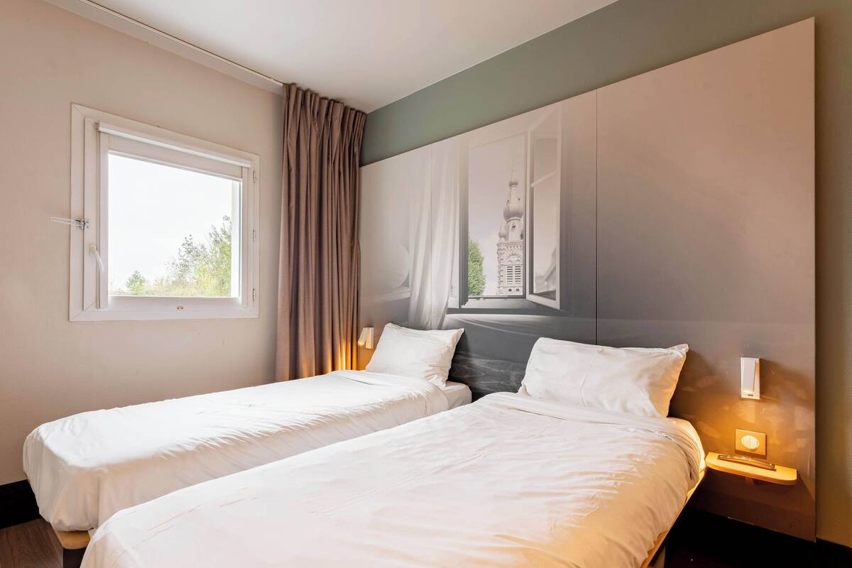 Habitación de hotel con dos camas, un ventanal grande, un mural en la pared y lámparas de noche.