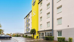 Un hotel con un llamativo letrero vertical amarillo, numerosas ventanas y un área de estacionamiento.
