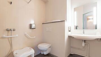 Et badeværelse med toilet, vask, spejl og en brusekabine med gelænder.