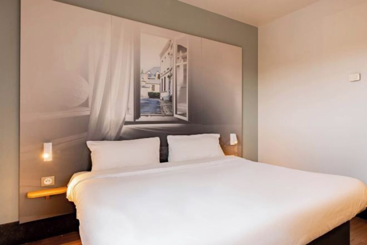 Una habitación de hotel con una cama grande, un cuadro de una escena callejera en la pared y una mesita de noche con una lámpara.
