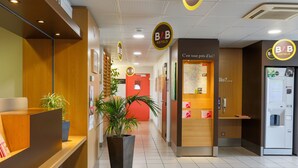 Zona de recepción de hotel con un mostrador de madera, una planta en maceta grande y una puerta roja que da a las habitaciones.