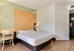 Ein modernes Hotelzimmer mit Bett, Schreibtisch, Sessel und Kleiderschrank.