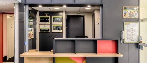 Un mostrador de recepción con superficie de madera, una puerta negra y carteles informativos en la pared.