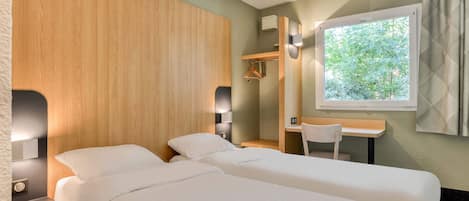 Habitación de hotel con dos camas, un escritorio, una silla, una ventana con vista a árboles y un cabecero de madera.