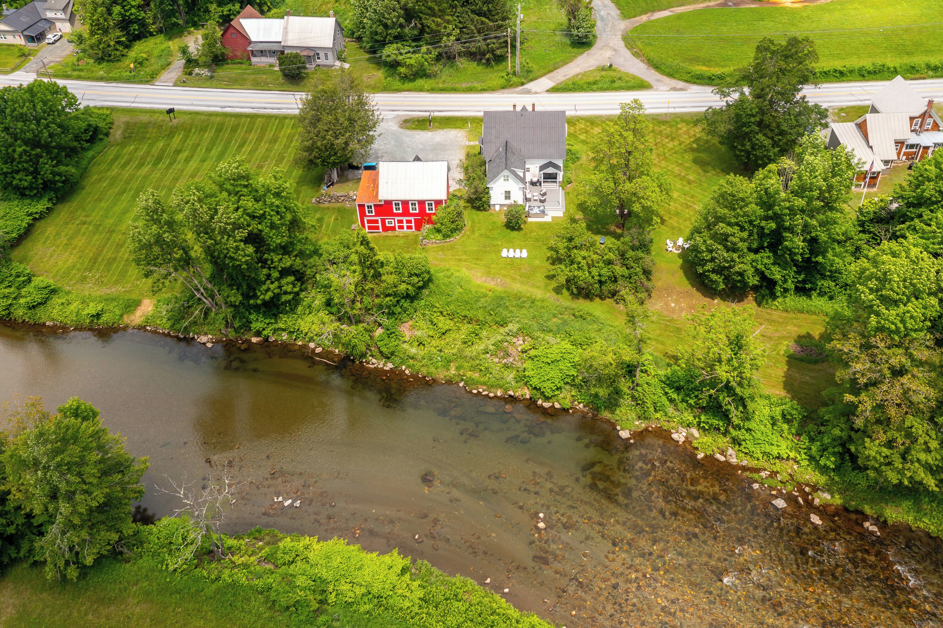 A rural landscape with a river, a red house, and a white house with a grey roof.