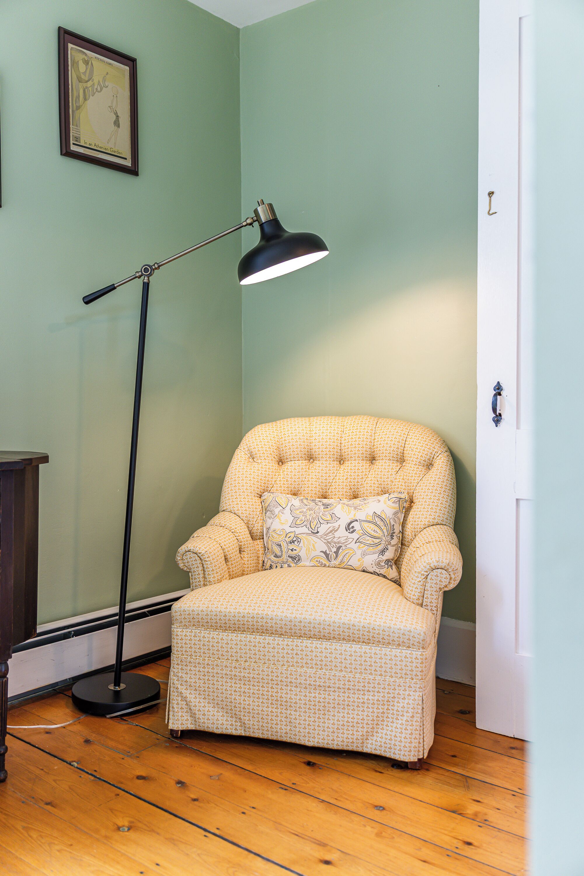 A corner room with a patterned armchair, a standing floor lamp, and a door.