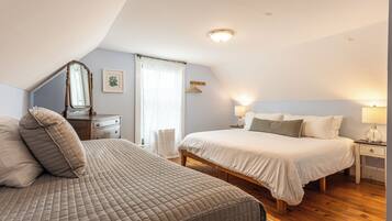 A bedroom with two beds, a dresser, a mirror, a bedside table with a lamp, and a window with curtains.