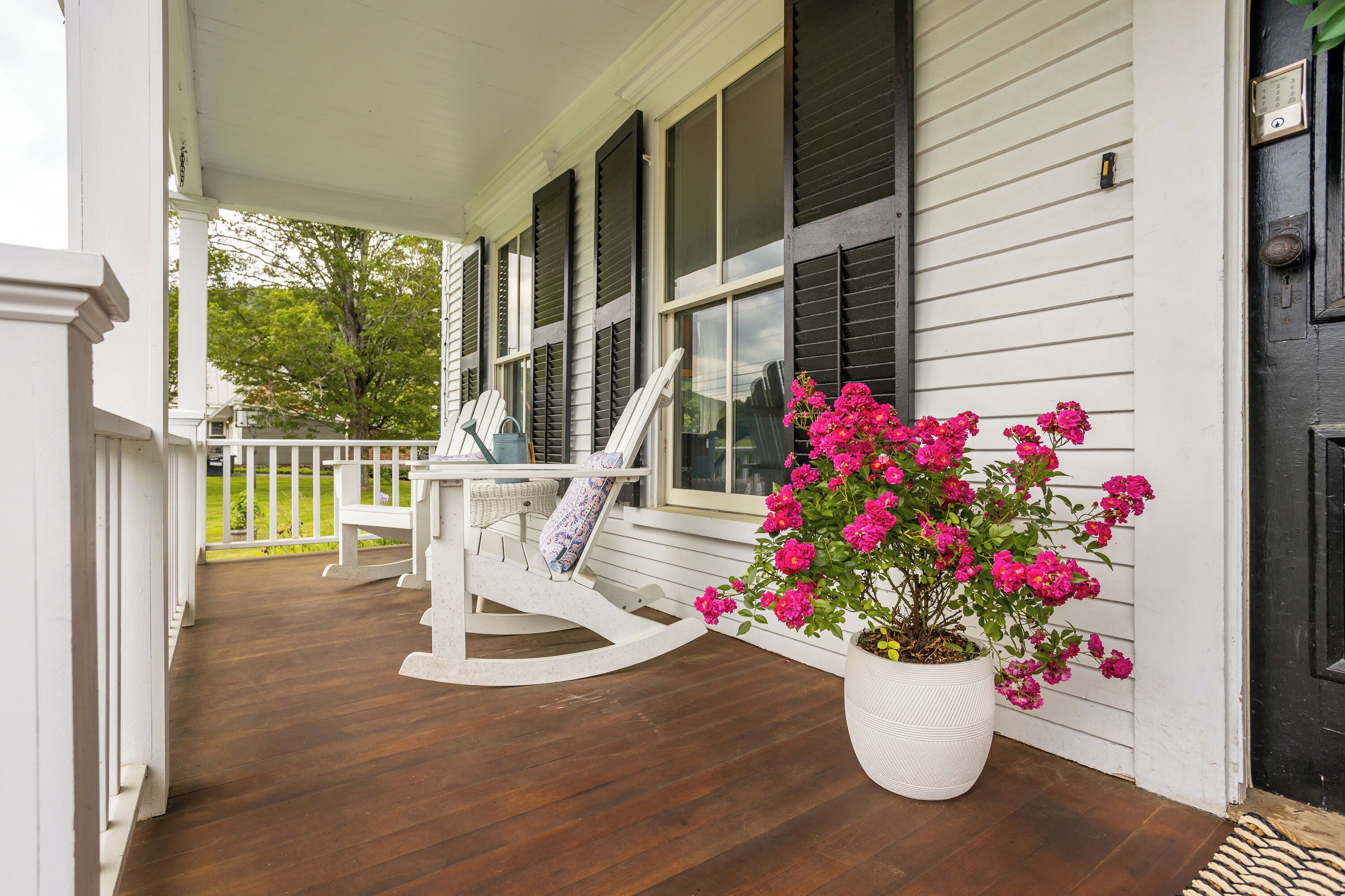 A porch with a rocking chair and a potted plant with pink flowers.