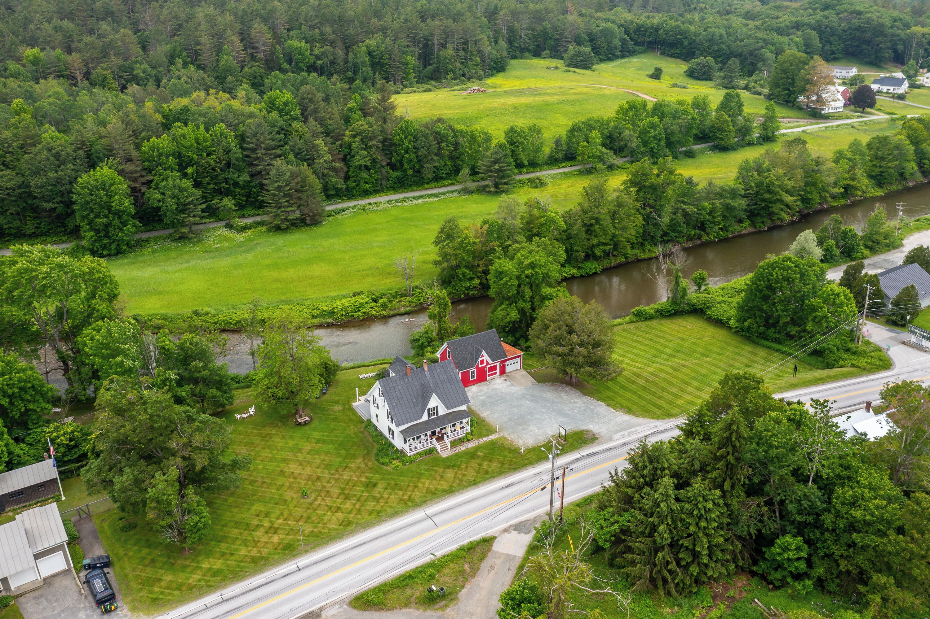 Une grande maison avec un garage rouge, entourée d’une pelouse bien entretenue et bordée par une rivière.