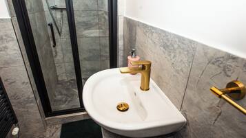 Un baño con lavamanos blanco, grifo dorado y cabina de ducha de vidrio.