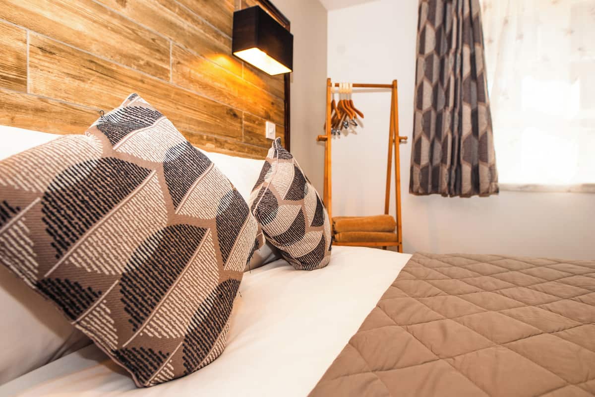 A bed with patterned pillows, a wooden headboard, and a hanging light fixture.