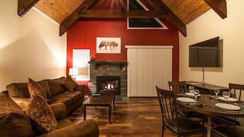 A living room with a fireplace, wooden ceiling beams, a dining area with a table set for four, and a red accent wall.