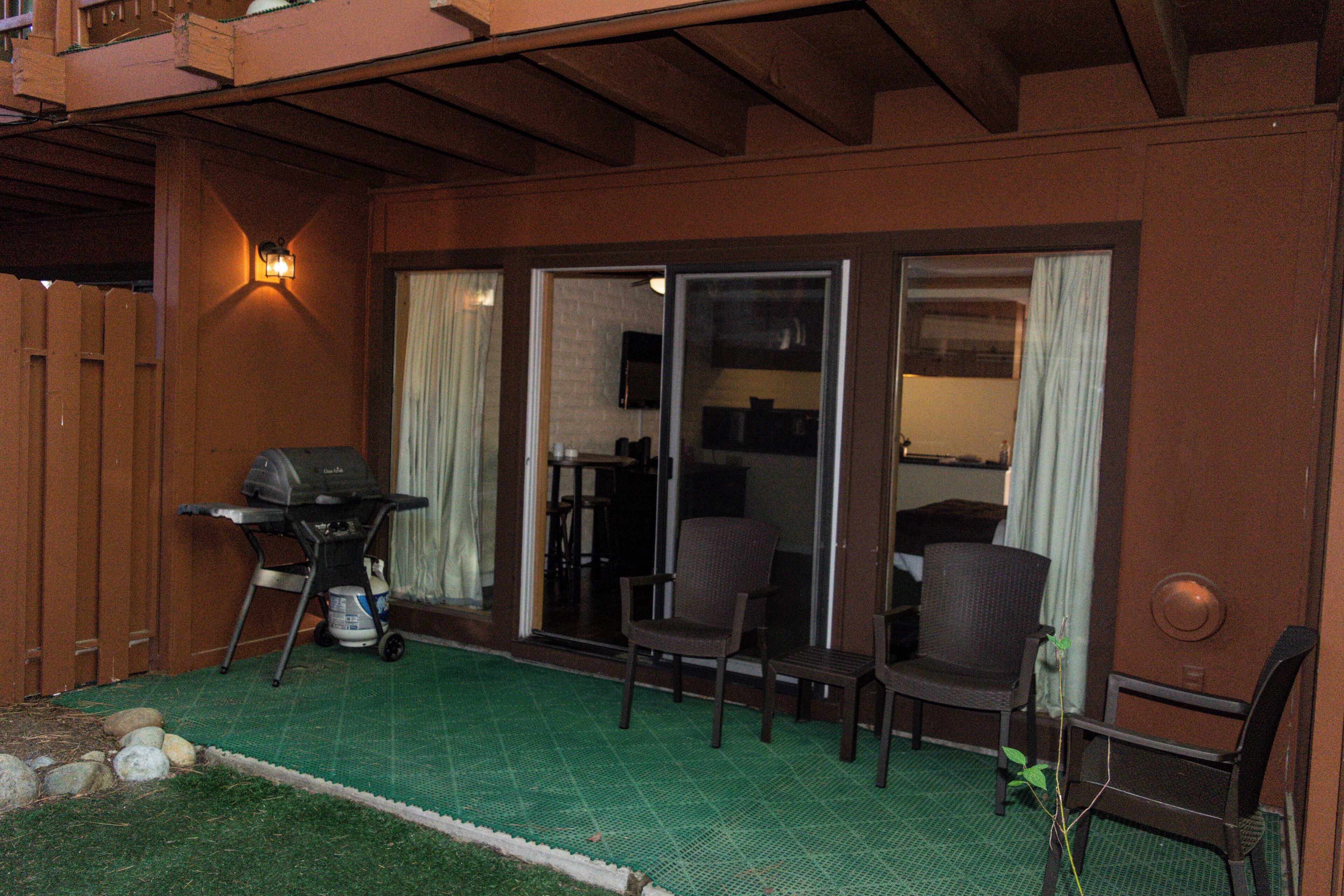 Un espace extérieur aménagé en terrasse, avec un barbecue, deux chaises et une petite table.