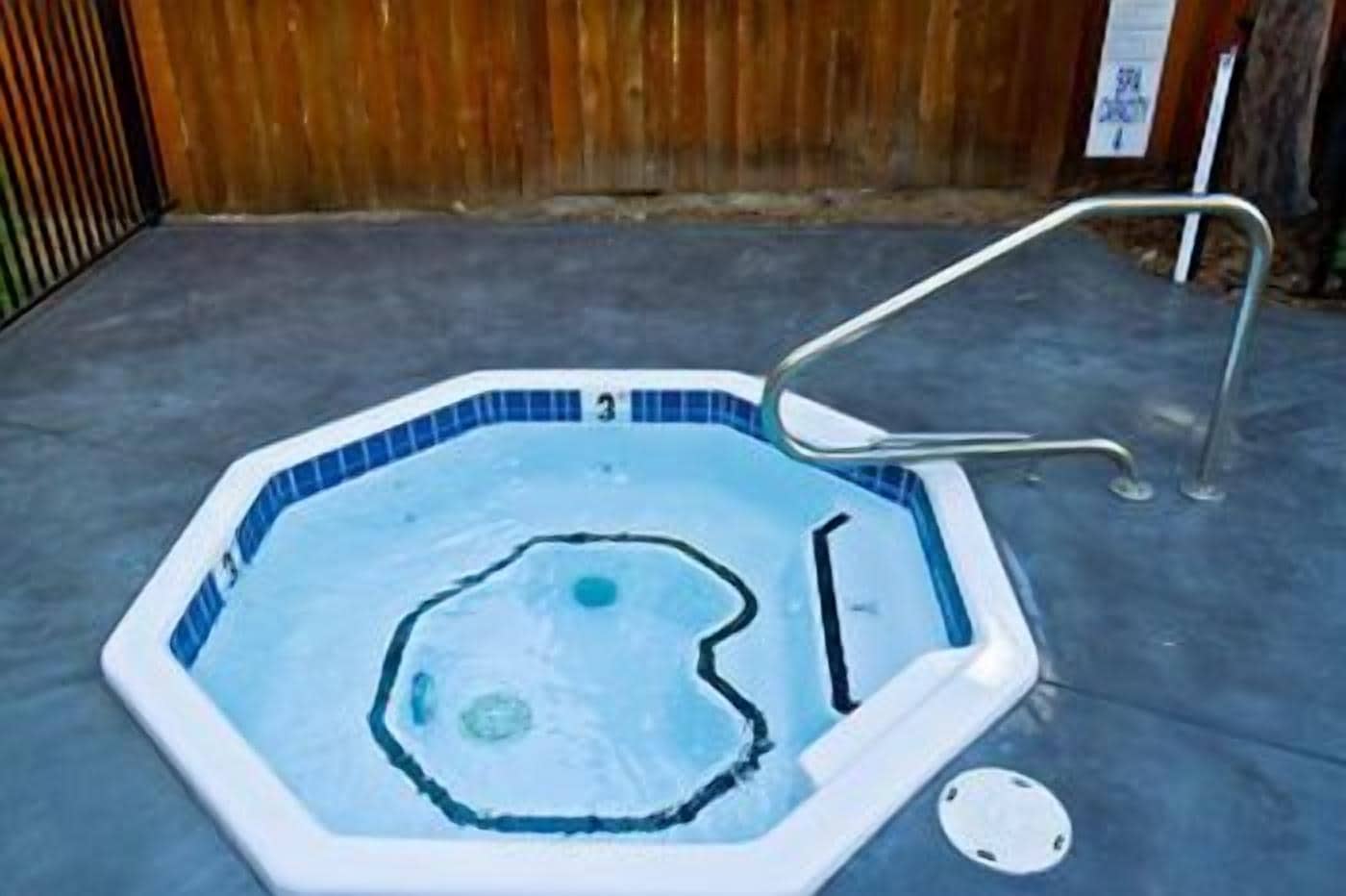 Un pequeño jacuzzi octogonal con una escalera metálica y un tapón de desagüe.
