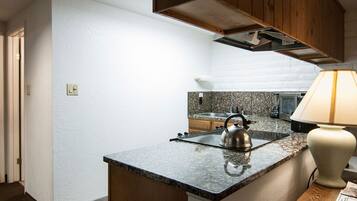 A compact kitchen with granite countertops, a kettle, a sink, and wooden cabinets.