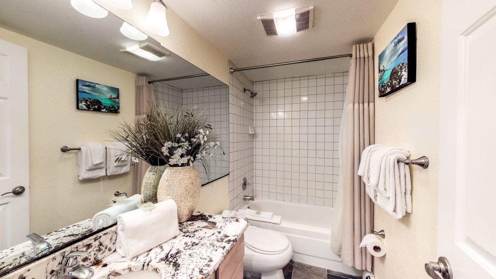 A bathroom with a bathtub, toilet, and sink. There are towels and a vase with flowers on the counter.