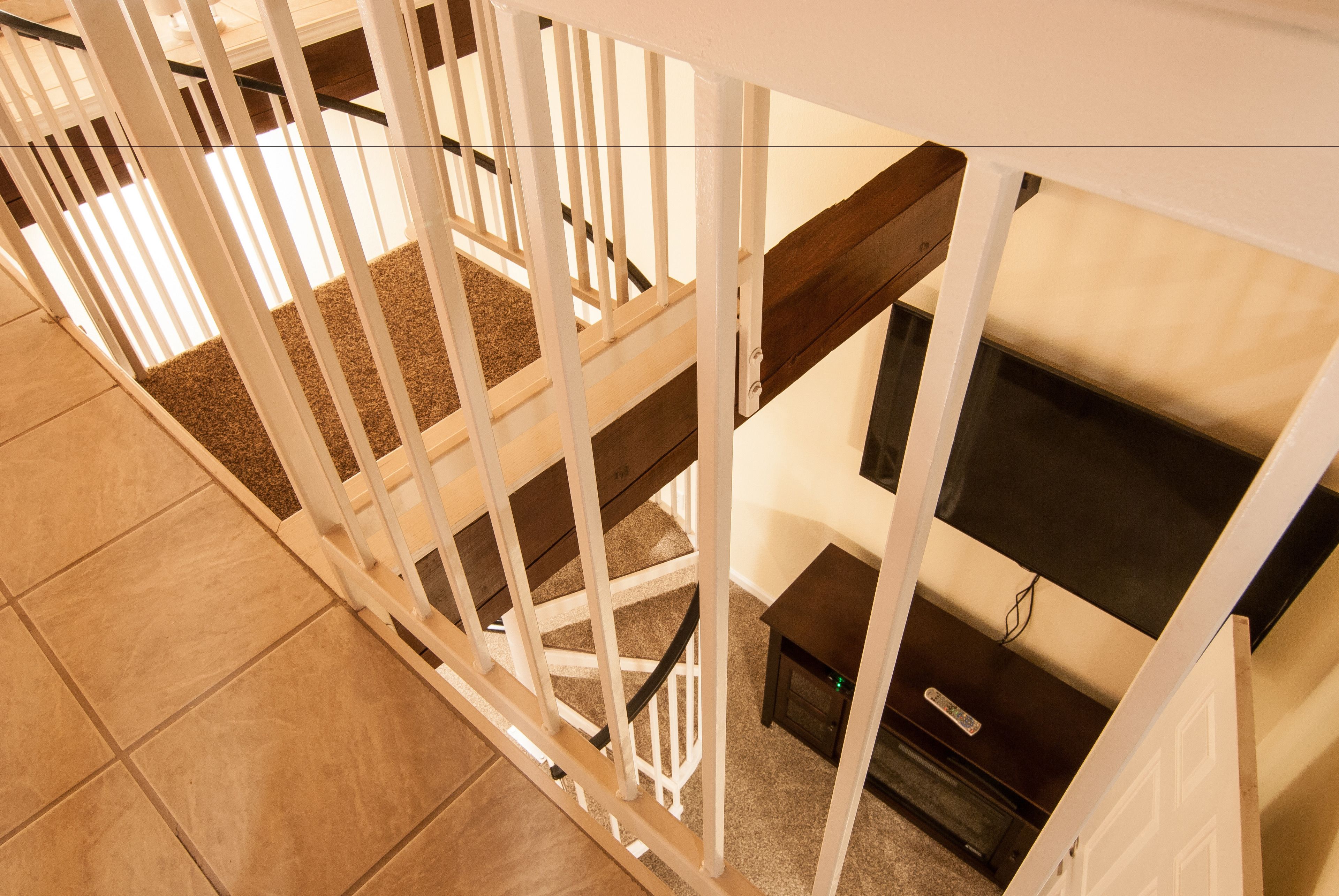 Un escalier avec des rampes blanches, des marches recouvertes de moquette et un plancher en bois foncé.