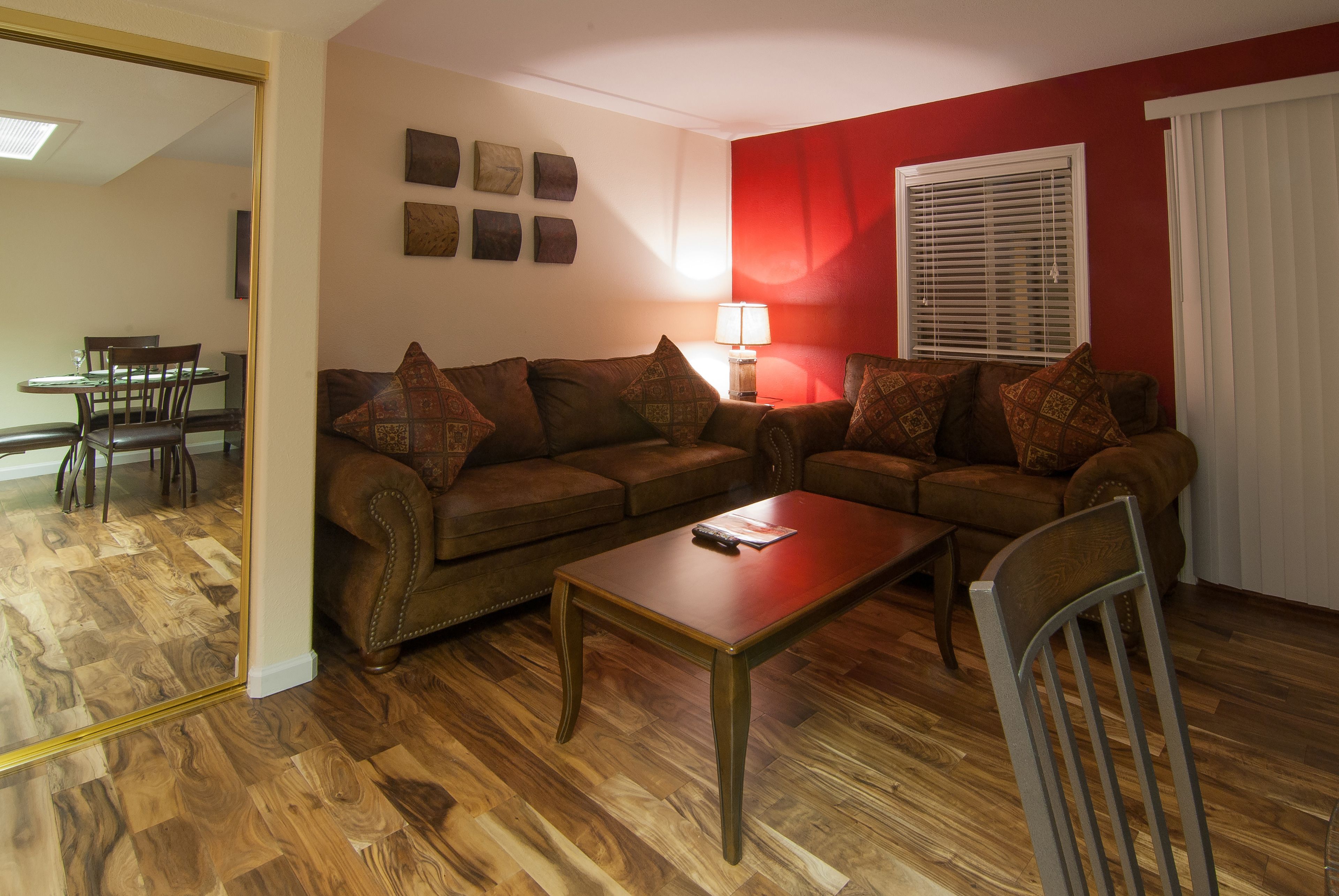 A living room with a brown sofa, a wooden coffee table, and a dining area with a table and chairs.