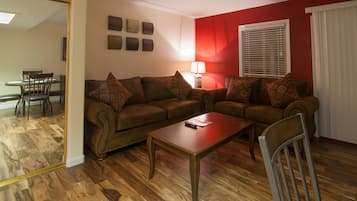 A living room with a brown sofa, a wooden coffee table, and a dining area with a table and chairs.