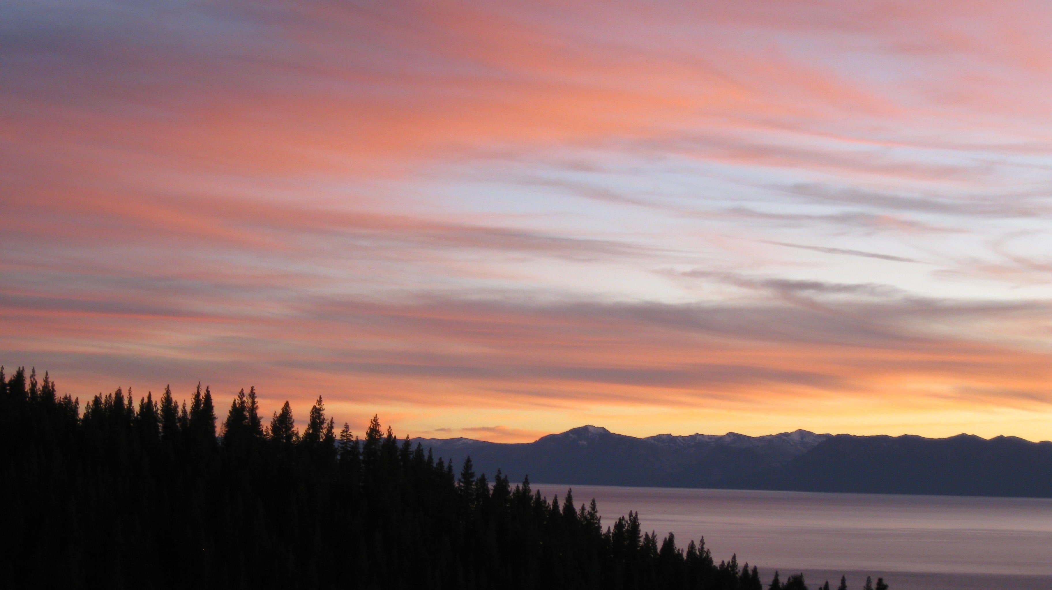 A mountainous landscape with a lake and forest at sunset.