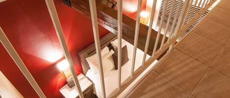 A bedroom with a red wall, a wooden bed frame, a nightstand, and a lamp.