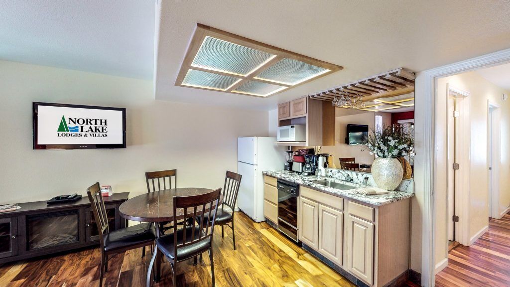 A compact kitchen with a dining area, wooden flooring, and a ceiling light fixture.
