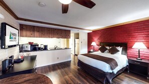 Une chambre d’hôtel moderne dotée d’un coin cuisine, d’un lit avec une tête de lit et d’un mur d’accent en briques rouges.