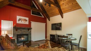 A living room with a fireplace, a dining area with a table and chairs, and a red wall with a mounted picture.