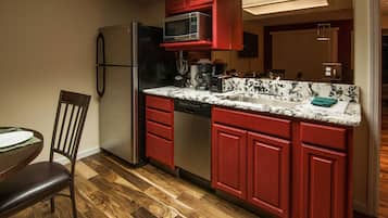 A compact kitchen with red cabinets, a stainless steel refrigerator, a microwave, and a dishwasher.