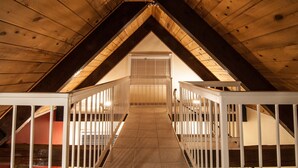 An attic room with a wooden ceiling, a staircase with white railings, and a window with blinds.