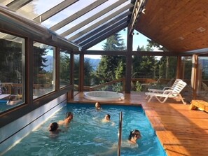 Una piscina interior con vistas despejadas del bosque y las montañas circundantes a través de amplios ventanales.